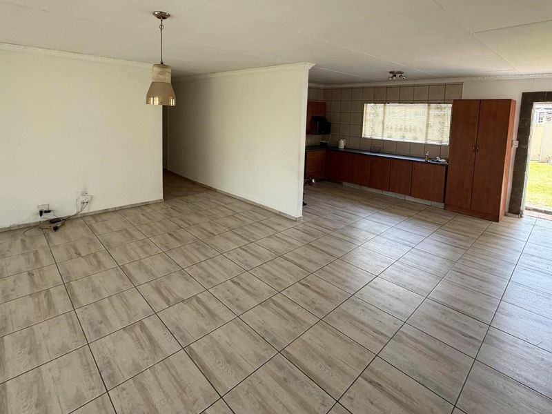 Spacious open-plan living area featuring neutral tiled flooring, integrated kitchen cabinetry, and direct access to the rear garden.