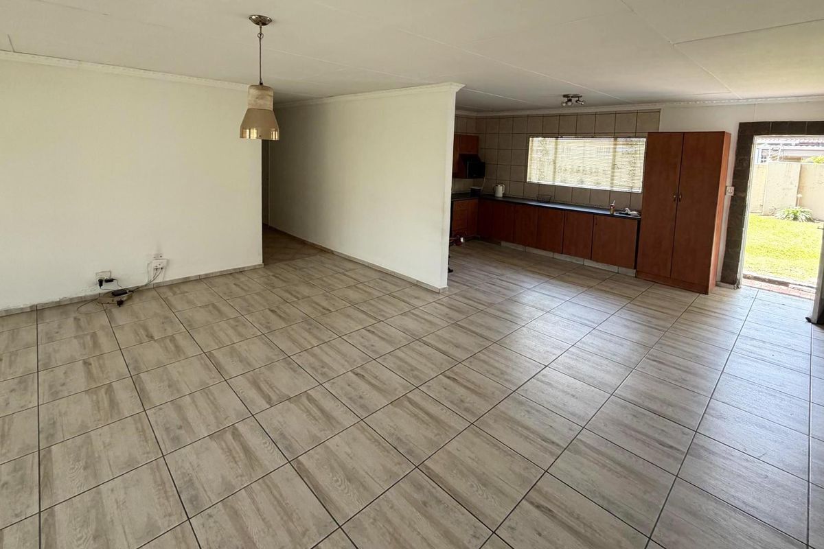 Spacious open-plan living area featuring neutral tiled flooring, integrated kitchen cabinetry, and direct access to the rear garden.