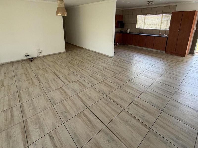 An open-plan living and kitchen area featuring wood-look tiled flooring, built-in cabinetry, and direct access to the rear garden.