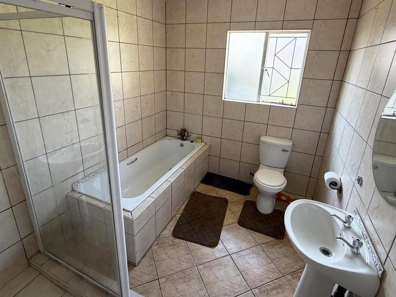 A functional bathroom featuring a built-in bathtub, separate shower enclosure, pedestal basin, and toilet with neutral wall and floor tiling.