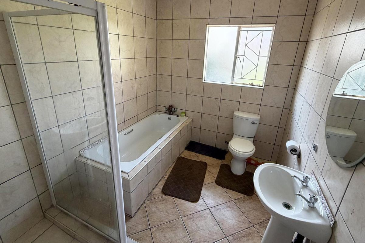 A functional bathroom featuring a built-in bathtub, separate shower enclosure, pedestal basin, and toilet with neutral wall and floor tiling.