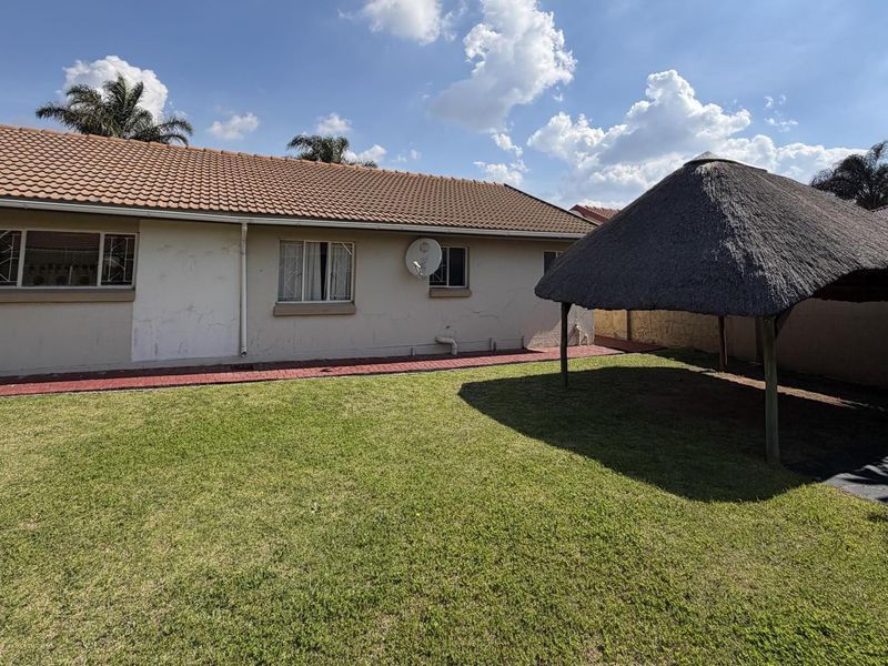 Rear view of the house featuring a lawn, paved walkway, and a thatched lapa structure in the garden.