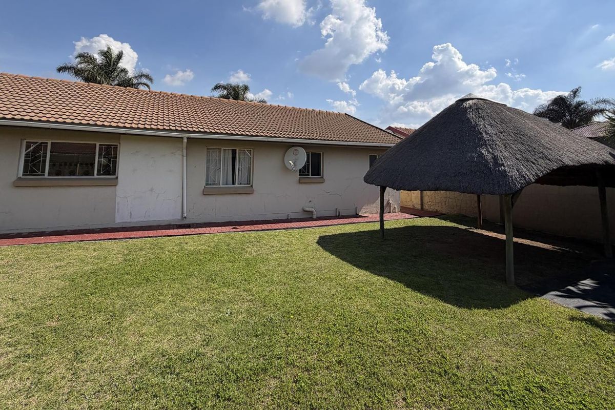 Rear view of the house featuring a lawn, paved walkway, and a thatched lapa structure in the garden.