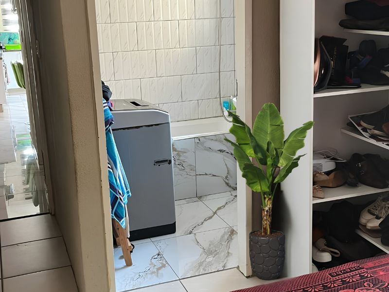 A bathroom featuring marble-effect floor tiles, wall tiling, and a shower-over-bath configuration, viewed from an adjacent room.