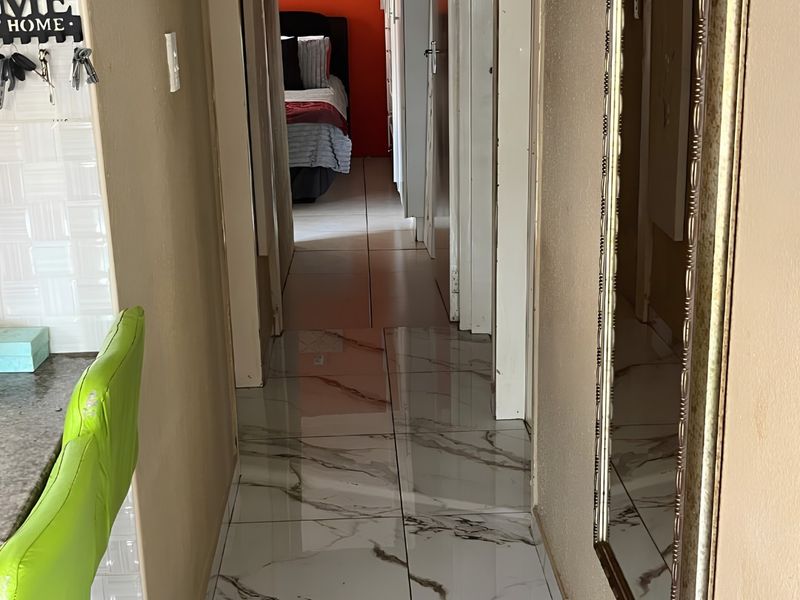 A hallway featuring modern marble-look floor tiles, providing access to adjacent rooms and connecting to the kitchen area.