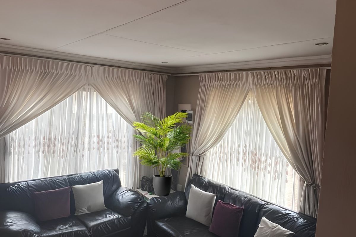 A comfortable living room featuring recessed downlights, decorative cornicing, and large windows dressed with elegant floor-to-ceiling curtains.