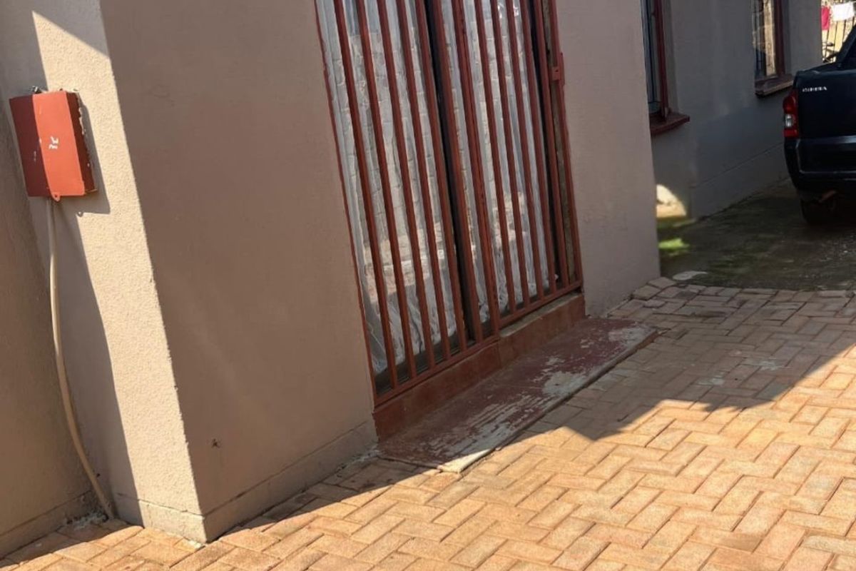 Rear exterior view featuring a paved patio area, security gate, and external electrical infrastructure.
