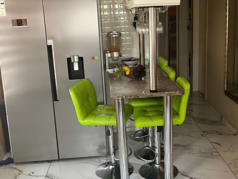 A compact kitchen area featuring a breakfast bar with metallic supports, tiled backsplash, and modern marble-look floor tiles.