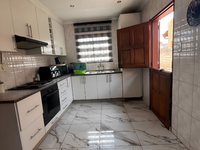 A modern kitchen featuring white cabinetry, marble-look floor tiles, a gas hob, electric oven, and a stable door leading to the exterior.