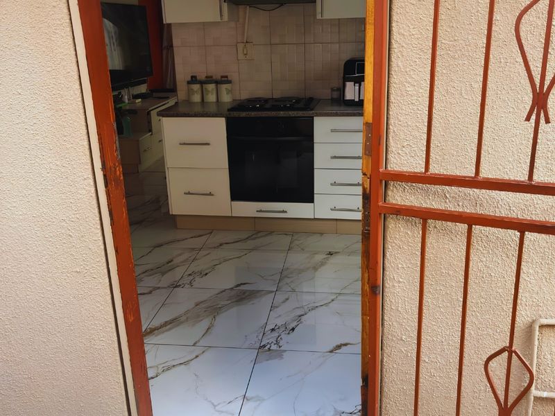 A functional kitchen featuring modern marble-look tiled flooring, built-in cabinetry, and integrated cooking appliances, viewed through a security gate entrance.