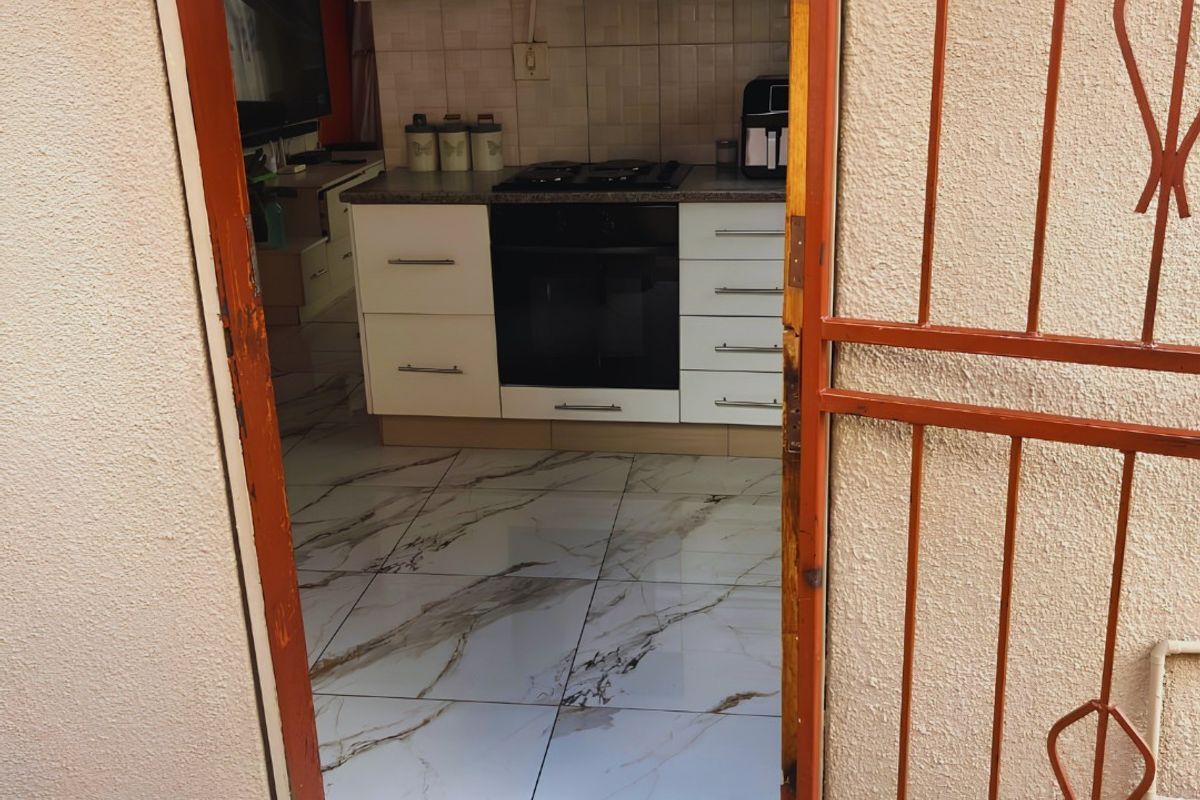 A functional kitchen featuring modern marble-look tiled flooring, built-in cabinetry, and integrated cooking appliances, viewed through a security gate entrance.