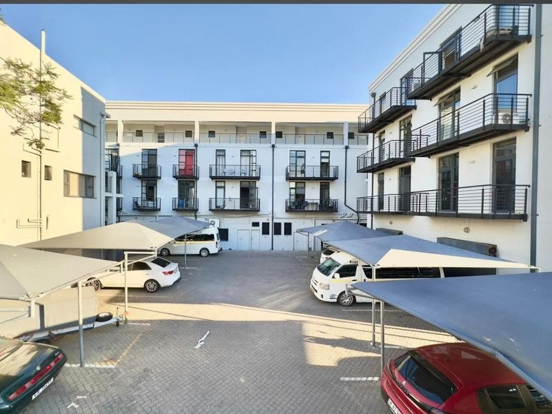 Exterior view of an apartment complex courtyard featuring paved parking bays with shade cloth carports and multiple levels of balconies with metal railings.