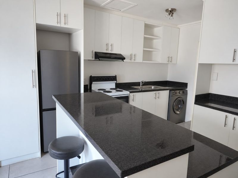 Modern kitchen featuring white cabinetry, dark granite countertops, integrated stove with extractor fan, and dedicated space for laundry appliances.