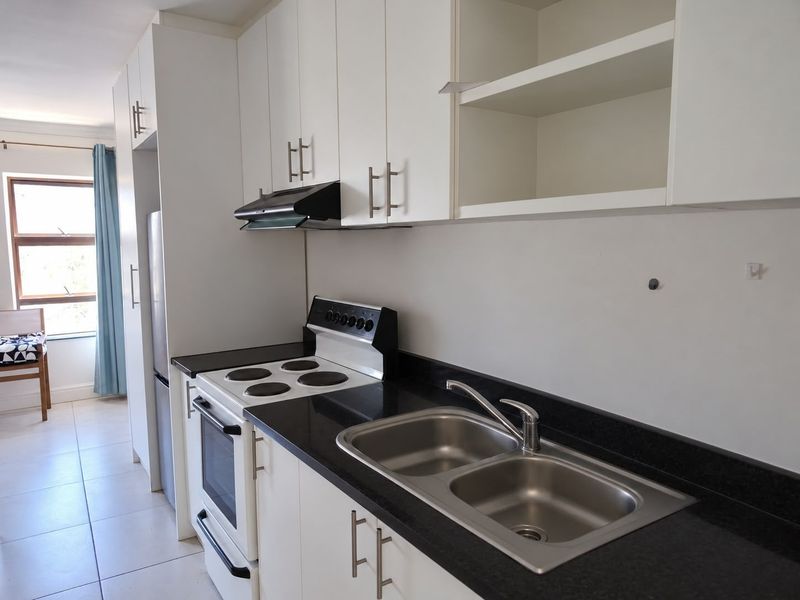 A functional kitchen featuring white cabinetry, black granite countertops, a stainless steel double sink, and a freestanding electric stove with an extractor fan.