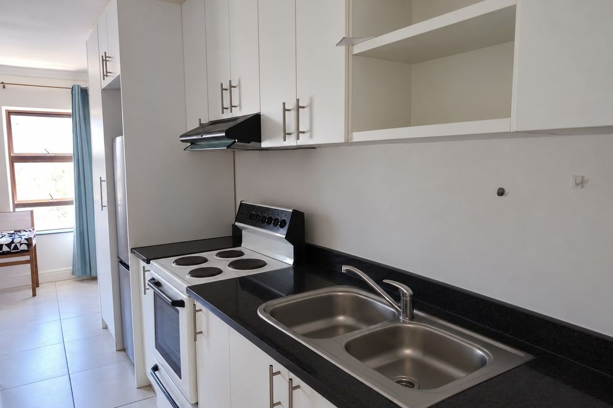 A functional kitchen featuring white cabinetry, black granite countertops, a stainless steel double sink, and a freestanding electric stove with an extractor fan.