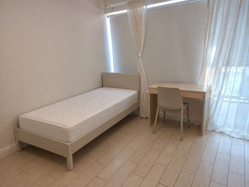 A bright and neutral bedroom featuring light-toned tiled flooring and large windows with sheer curtains, offering a clean and minimalist living space.