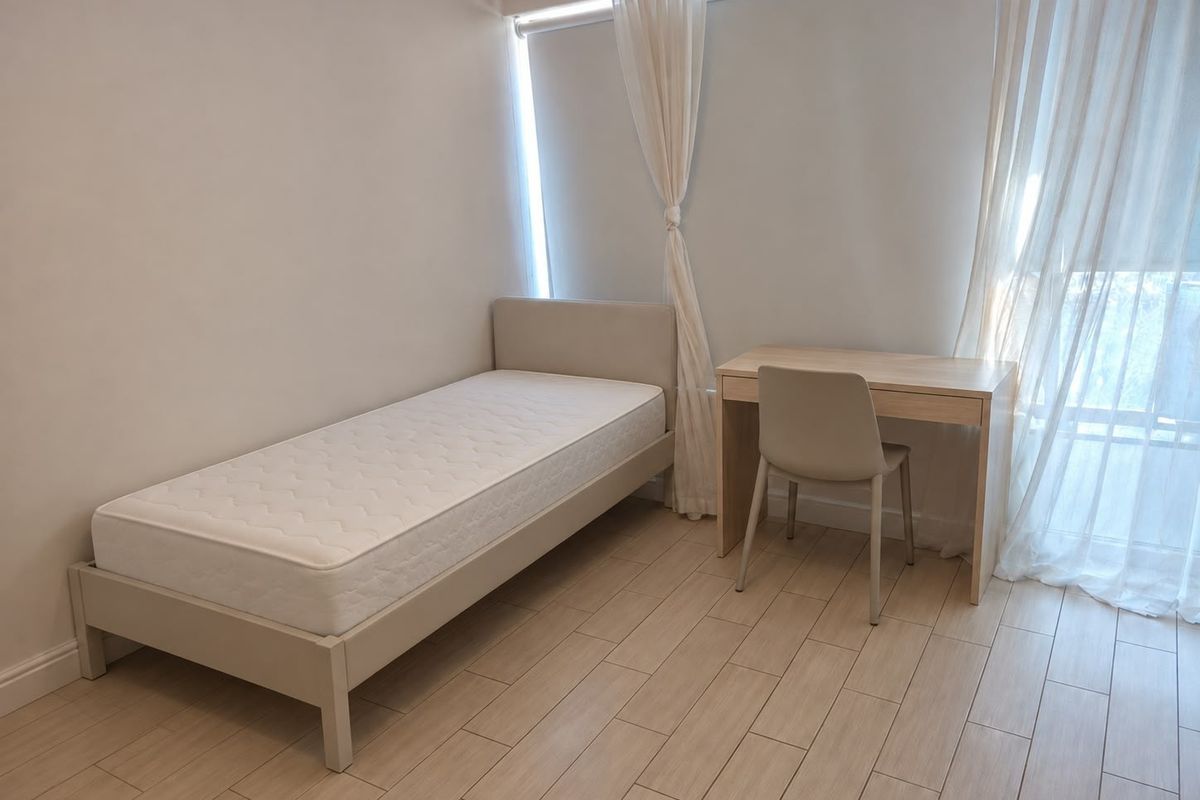 A bright and neutral bedroom featuring light-toned tiled flooring and large windows with sheer curtains, offering a clean and minimalist living space.