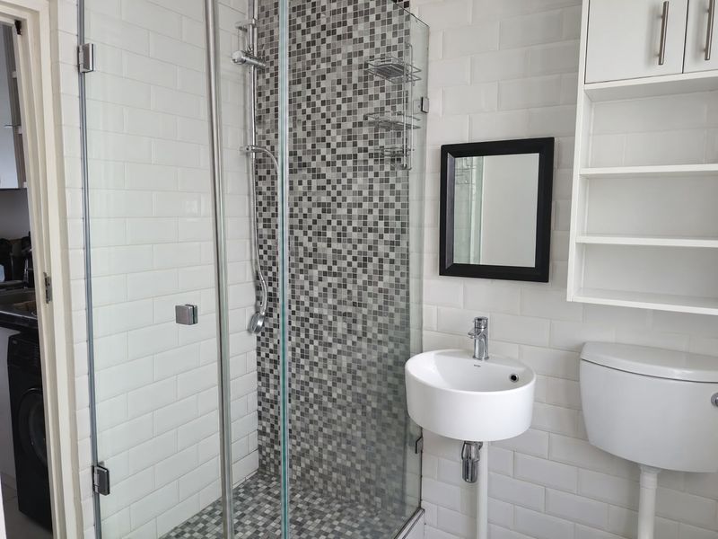 A clean, modern bathroom featuring a glass-enclosed shower with mosaic tile accents, a wall-mounted basin, and built-in storage shelving.