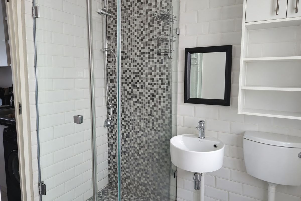 A clean, modern bathroom featuring a glass-enclosed shower with mosaic tile accents, a wall-mounted basin, and built-in storage shelving.