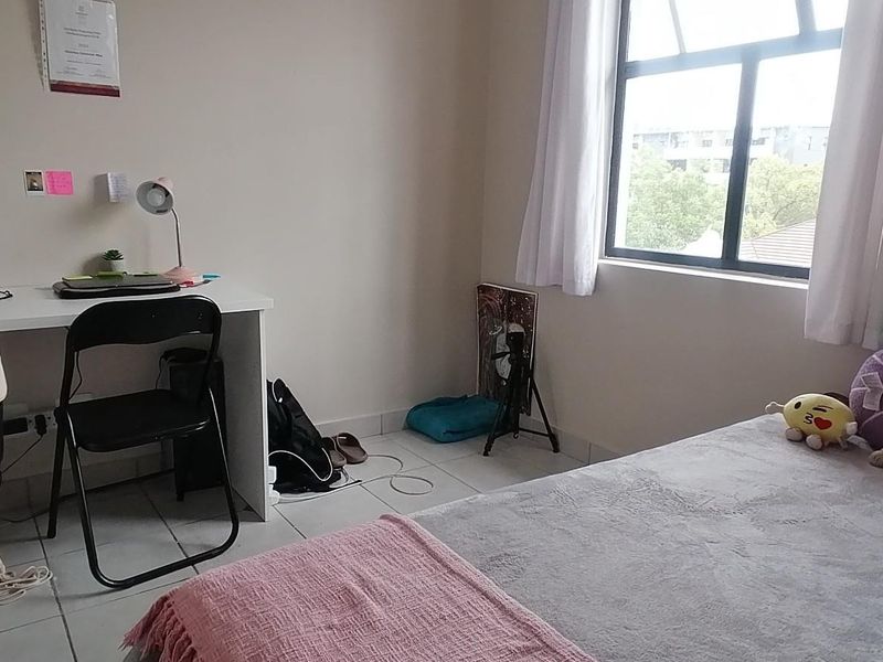 A functional bedroom featuring tiled flooring and a large window providing natural light, suitable for a comfortable living space.