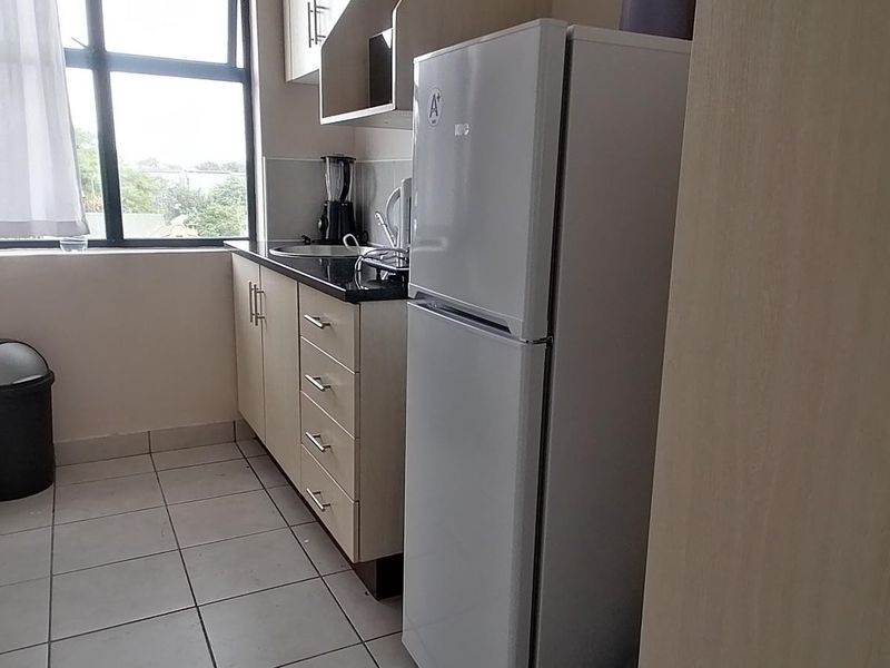 A compact kitchen featuring built-in cabinetry, laminate countertops, a stainless steel sink, and tiled flooring, offering a functional layout for an apartment.