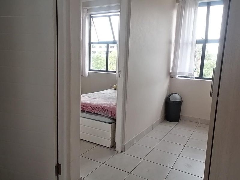 A functional hallway area with tiled flooring and natural light, providing access to an adjacent bedroom and bathroom.