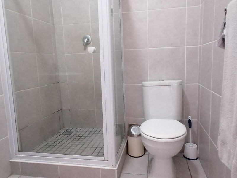 A functional bathroom featuring a shower enclosure, pedestal basin, and toilet with neutral wall and floor tiling.