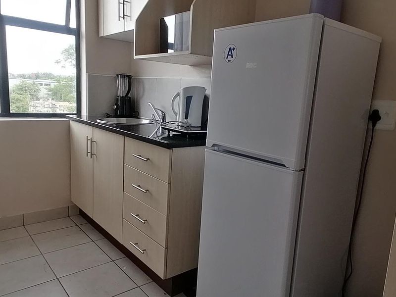 Compact kitchen featuring light-toned built-in cabinetry, granite countertops, a stainless steel sink, and tiled flooring with natural light from a large window.