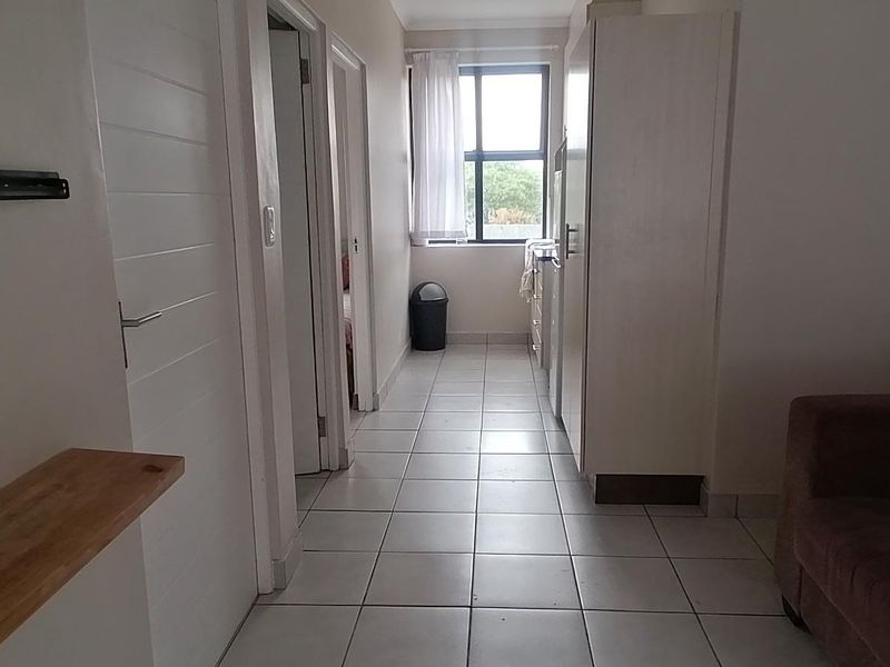 A functional hallway featuring tiled flooring, built-in storage cupboards, and access to adjacent rooms, leading towards a windowed area.