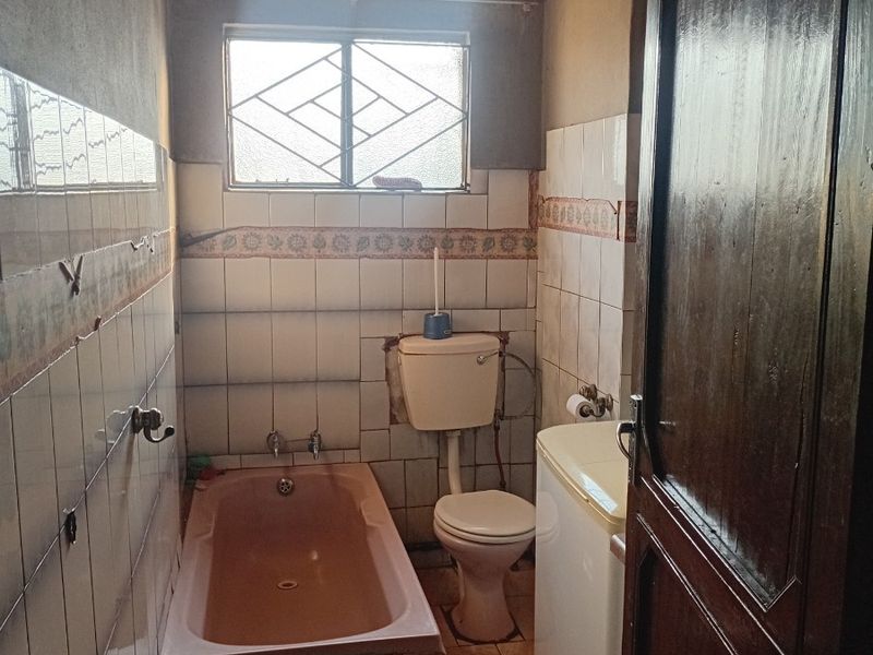 A dated bathroom featuring a built-in bathtub, toilet, and tiled finishes, requiring renovation to update the fixtures and address ceiling and wall surface wear.