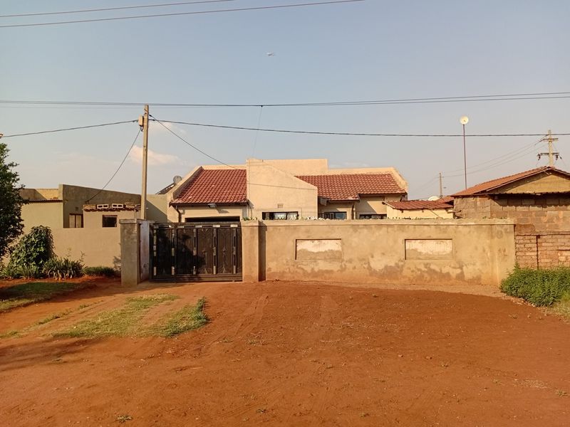 Front view of a residential property featuring a tiled roof house, a metal driveway gate, and a perimeter wall.