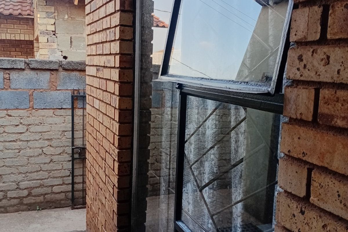 A view of the rear exterior featuring face brick walls, a top-hung window with security bars, and concrete paving.