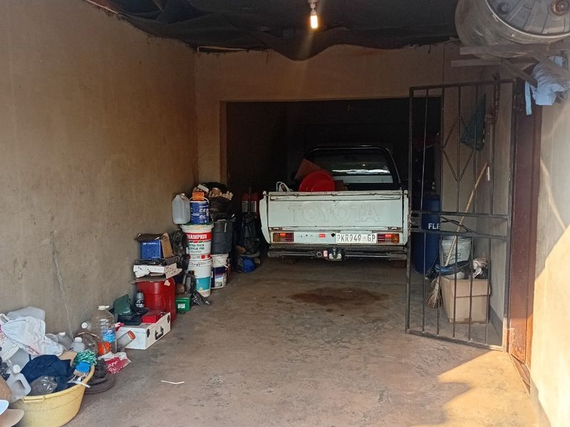A functional garage space featuring concrete flooring, a metal security gate, and overhead lighting, currently used for storage.