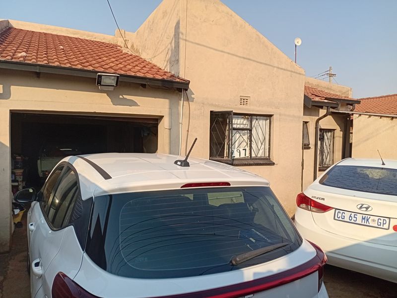Front elevation of a residential property featuring a garage, terracotta roof tiles, and security bars on the windows.