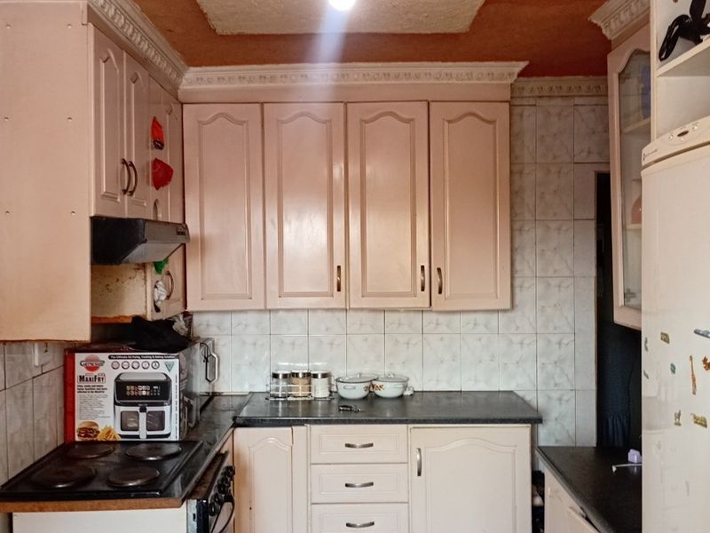 A compact kitchen featuring dated cabinetry, tiled backsplash, and a textured ceiling with a decorative rose, offering potential for a modern renovation.