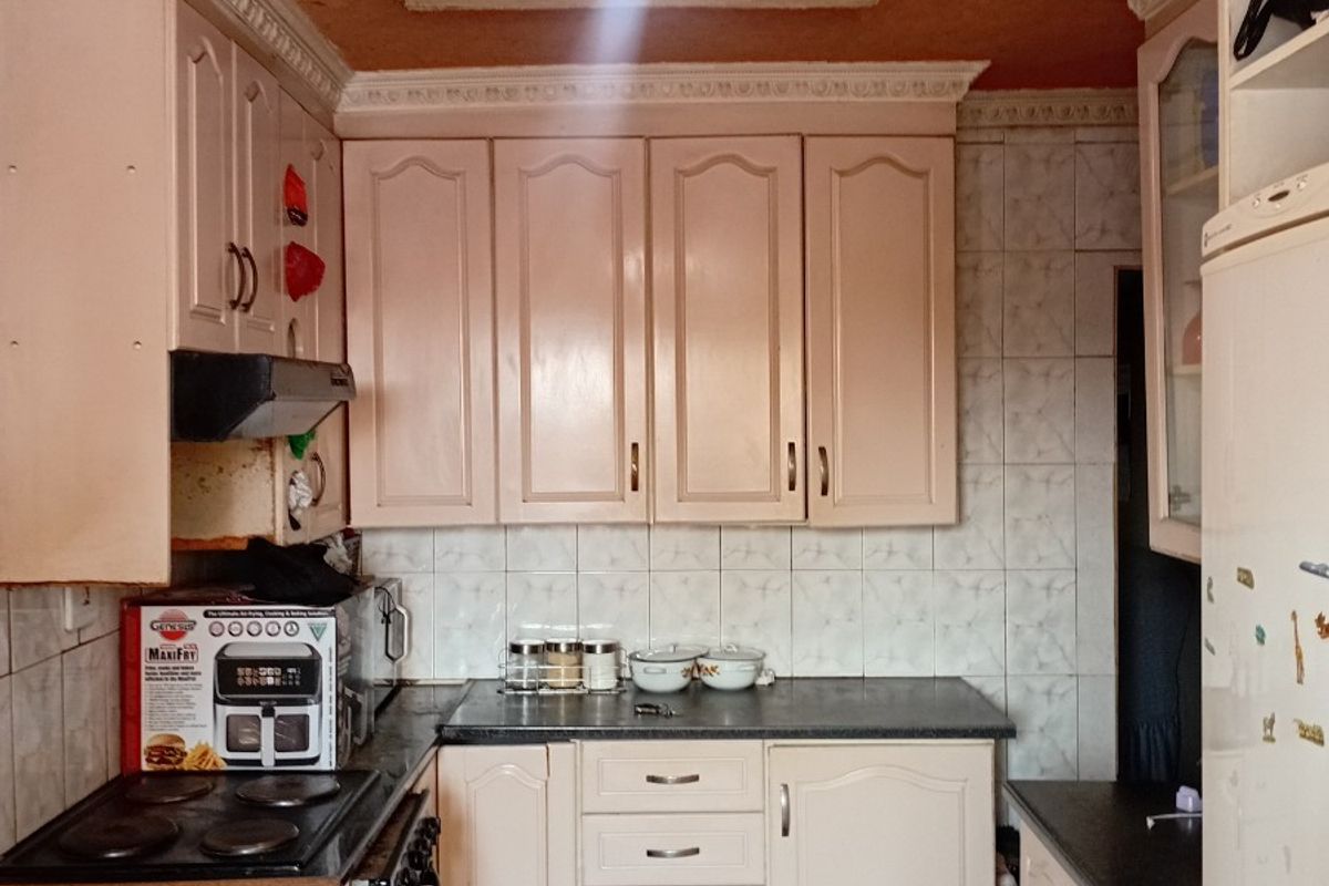 A compact kitchen featuring dated cabinetry, tiled backsplash, and a textured ceiling with a decorative rose, offering potential for a modern renovation.