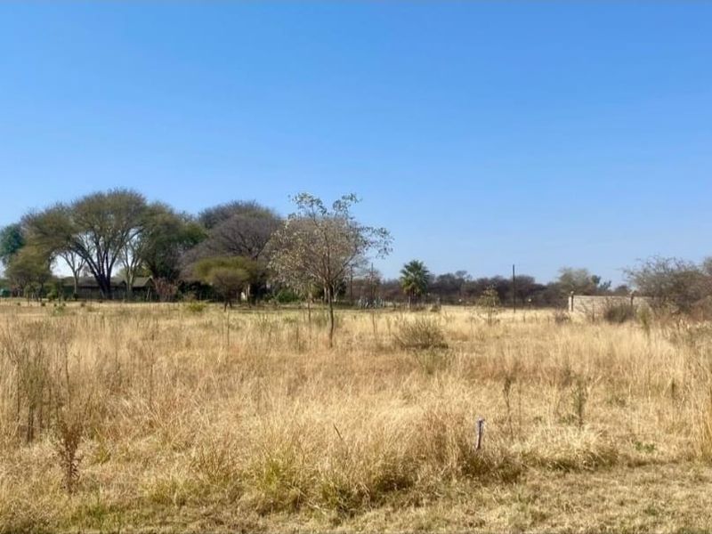 A view of a vacant residential plot featuring natural grass cover and mature trees, suitable for future development.