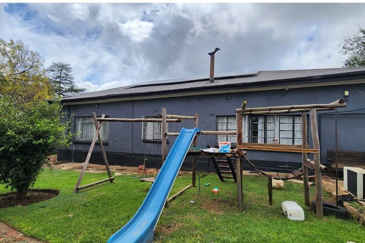 Rear view of the property featuring a corrugated metal roof with solar panels, security-barred windows, and a garden area.