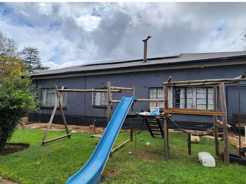 Rear view of the property featuring a corrugated metal roof with solar panels, security-barred windows, and a garden area.