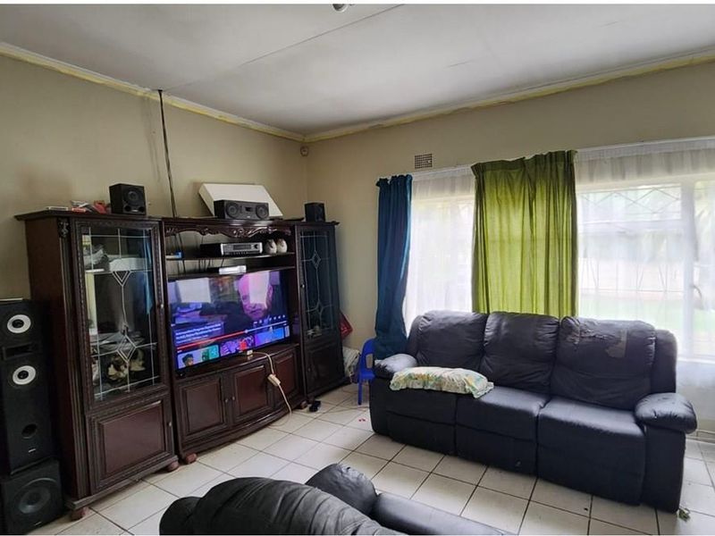 A living room featuring tiled flooring and security burglar bars on the windows, requiring some ceiling maintenance and cosmetic updates.
