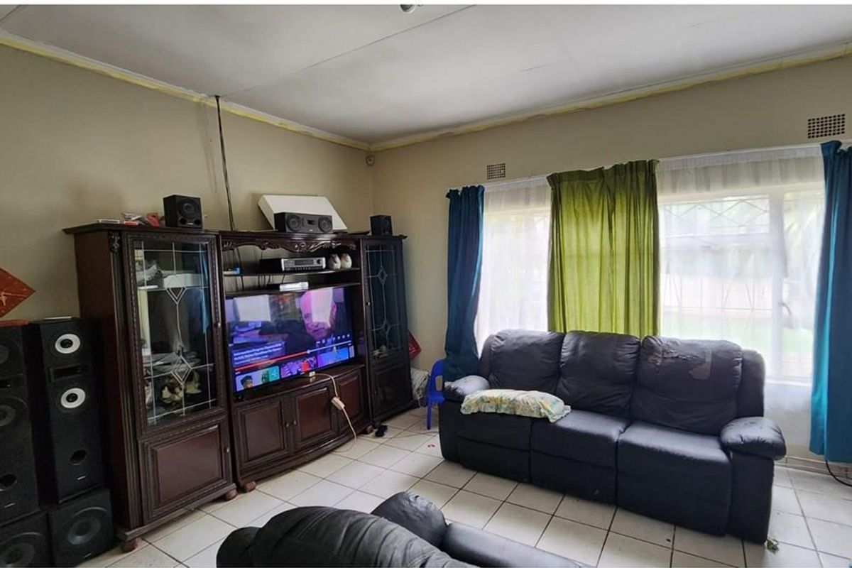 A living room featuring tiled flooring and security burglar bars on the windows, requiring some ceiling maintenance and cosmetic updates.