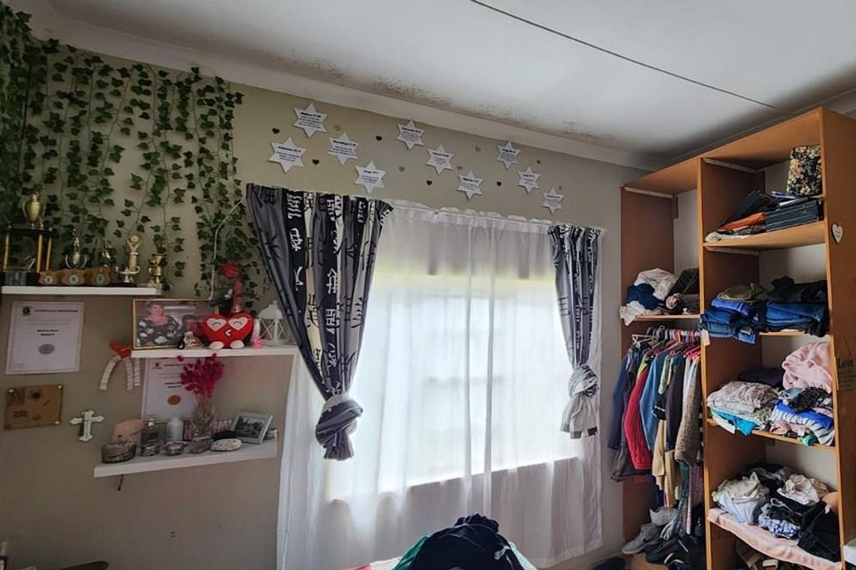 A bedroom featuring a built-in shelving unit and a window, showing visible signs of ceiling water damage requiring attention.