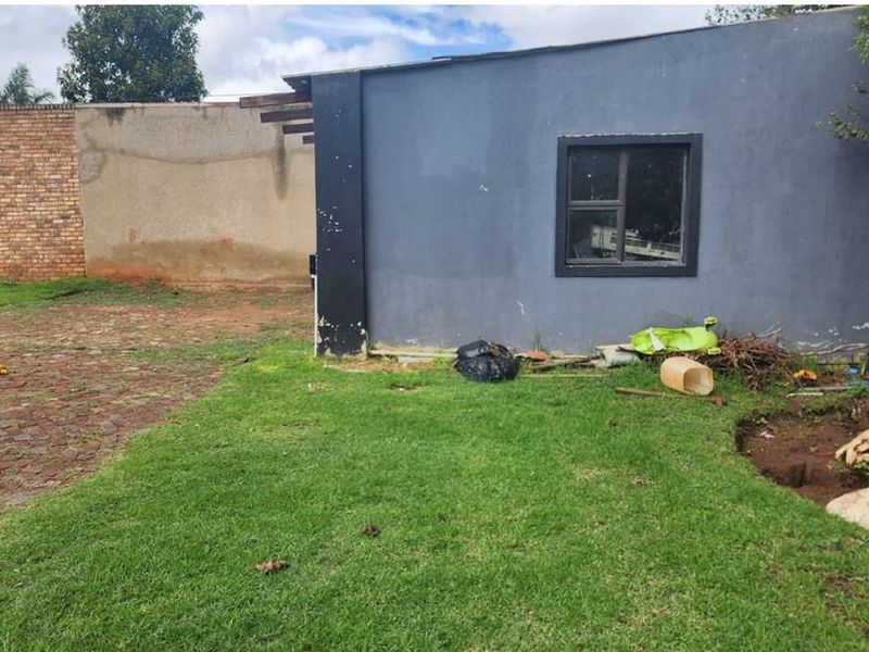 Rear exterior view of the property featuring a lawn, paved driveway area, and a grey painted structure with an aluminium window.
