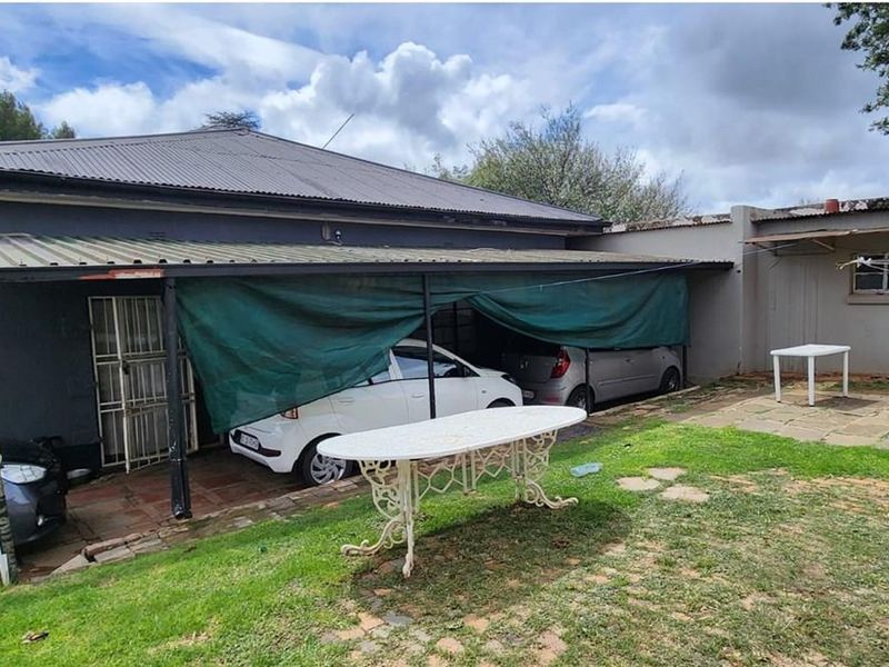 Rear exterior view of the property featuring a covered carport area, paved patio space, and established garden grounds.