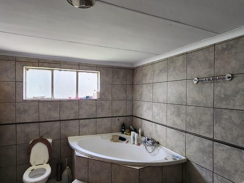 A functional bathroom featuring a corner bathtub, toilet, and full-height wall tiling. The space would benefit from modern updates to finishes and fixtures.