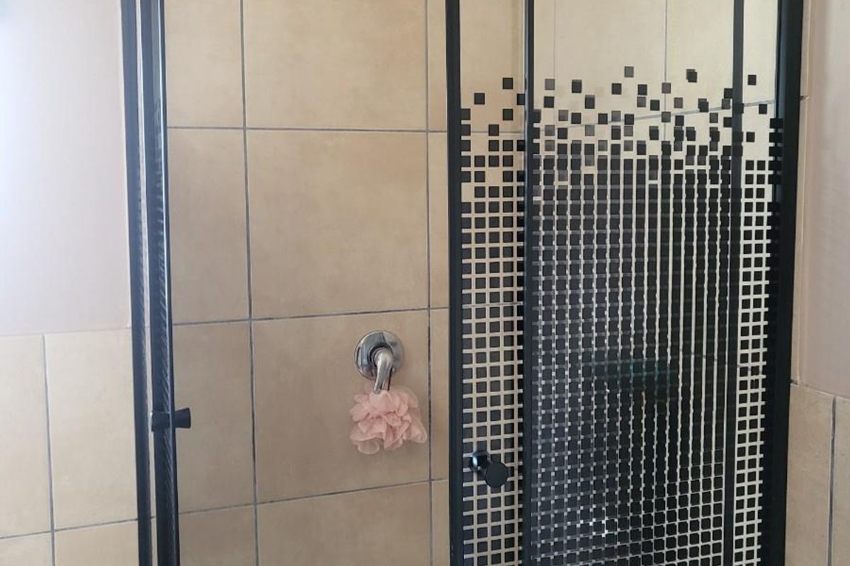 A shower enclosure featuring beige wall tiles, a black-framed glass door with a decorative pixelated pattern, and a chrome shower head.