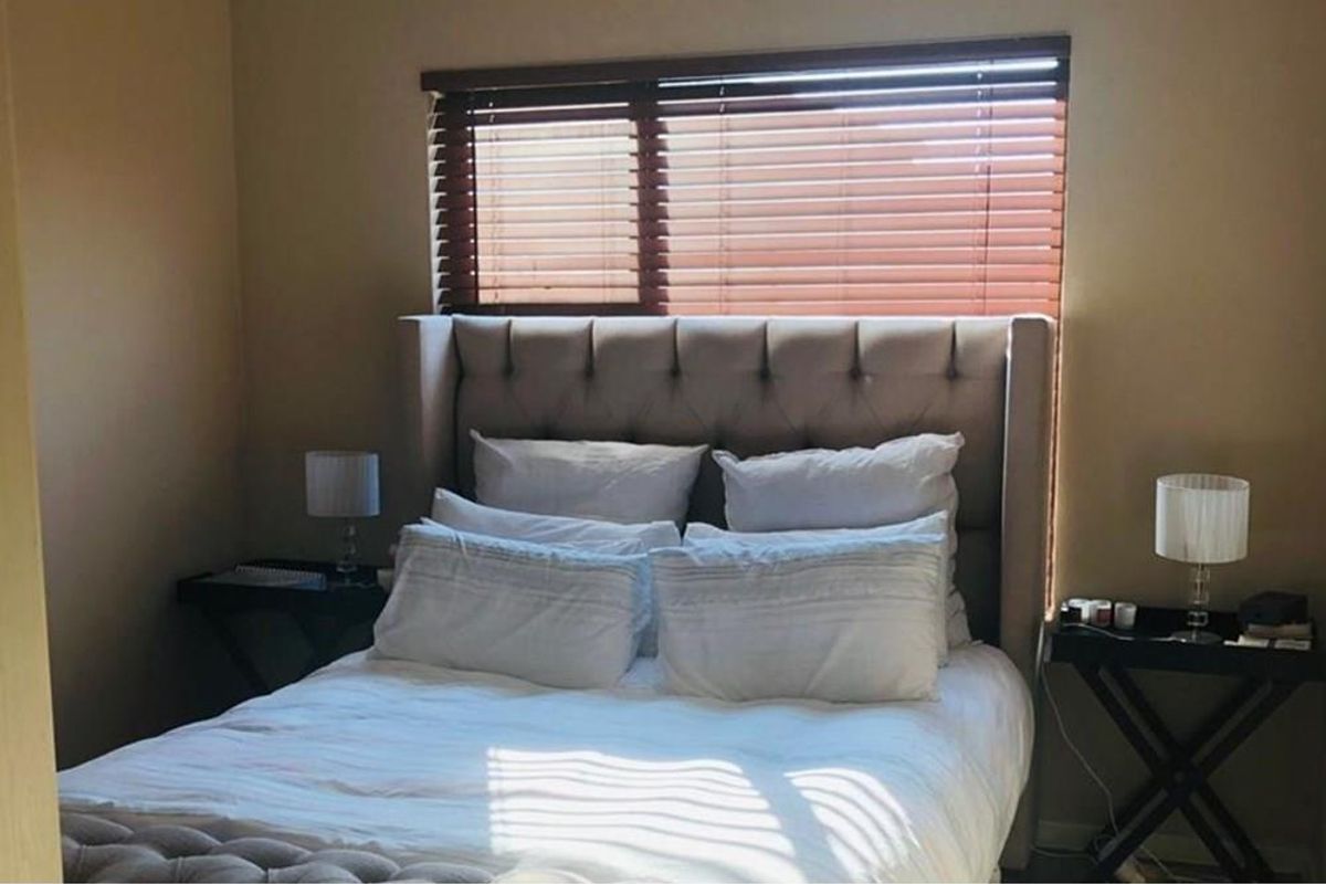 A cozy bedroom featuring a tufted headboard and wooden venetian blinds, providing a comfortable and private sleeping space.