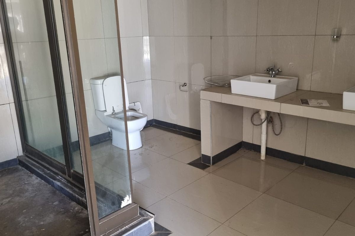 A functional bathroom featuring a double vanity with vessel sinks, a toilet, and a glass-enclosed shower area with tiled walls and flooring.