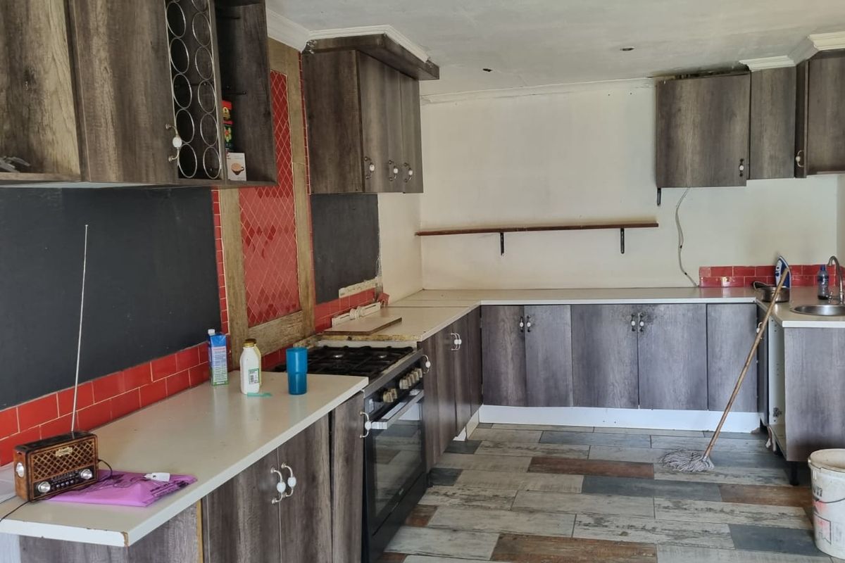 A kitchen space featuring wood-look cabinetry, a built-in oven with gas hob, and tiled flooring, currently requiring finishing touches and maintenance.