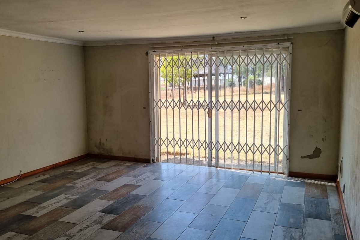 An empty living room featuring wood-look tiled flooring, a sliding glass door with a security gate, and wall-mounted air conditioning unit.
